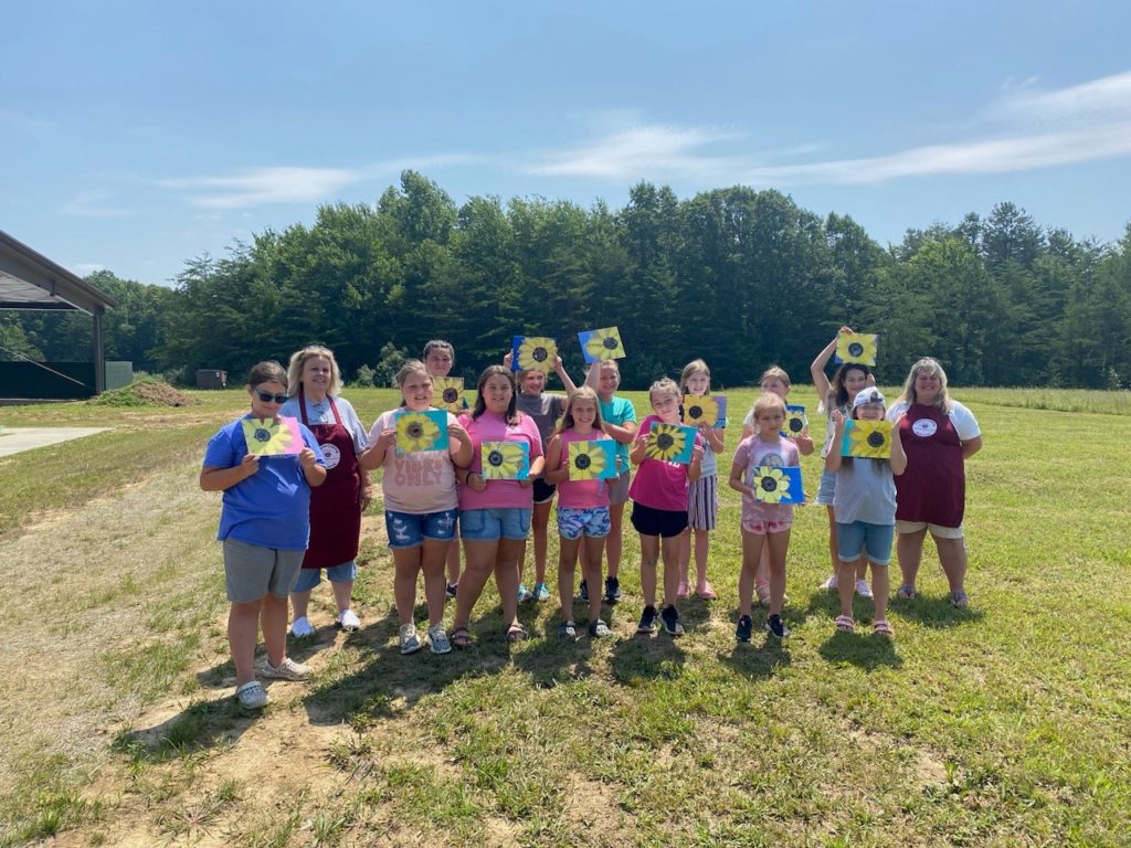 Group of girls showing off the paintings they made at day camp.