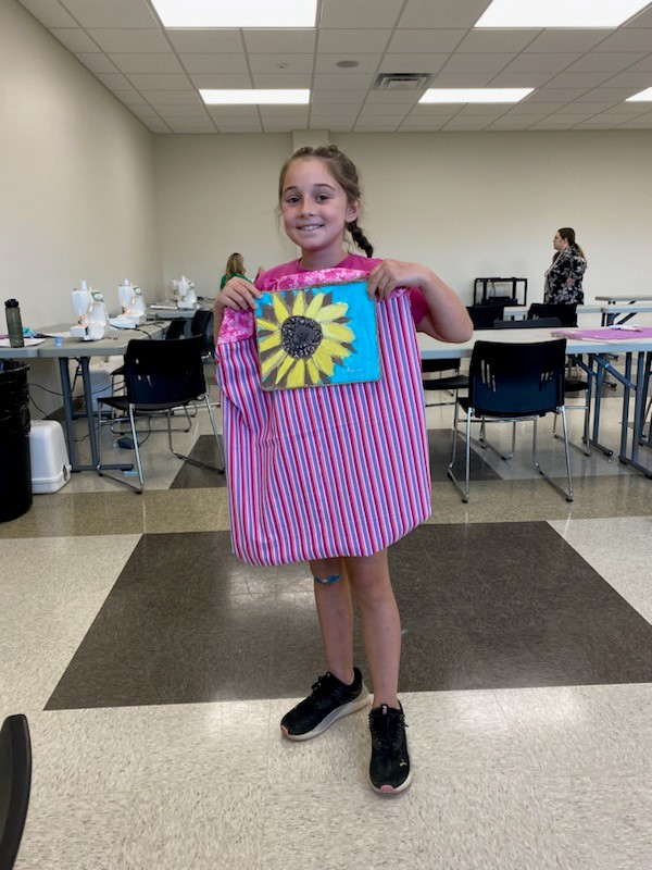 Young girl holding up the painting and pillow case she made during day camp.