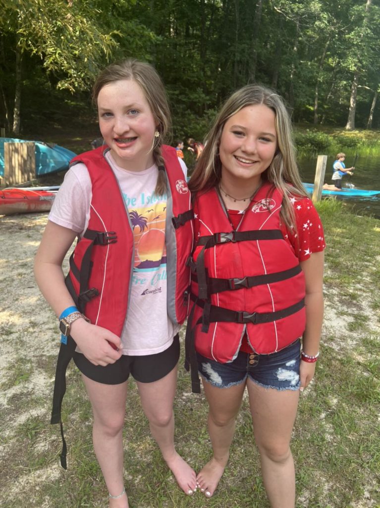 Two students in life jackets with kayaks behind them