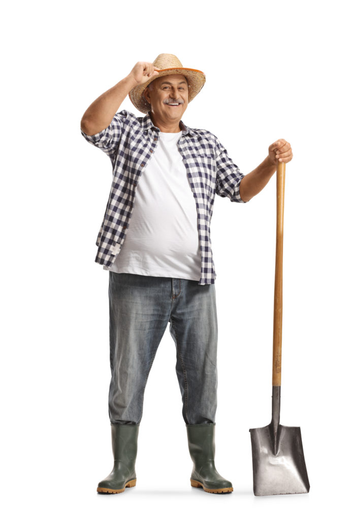 Full length portrait of a happy mature farmer with a shovel greeting with hat isolated on white background