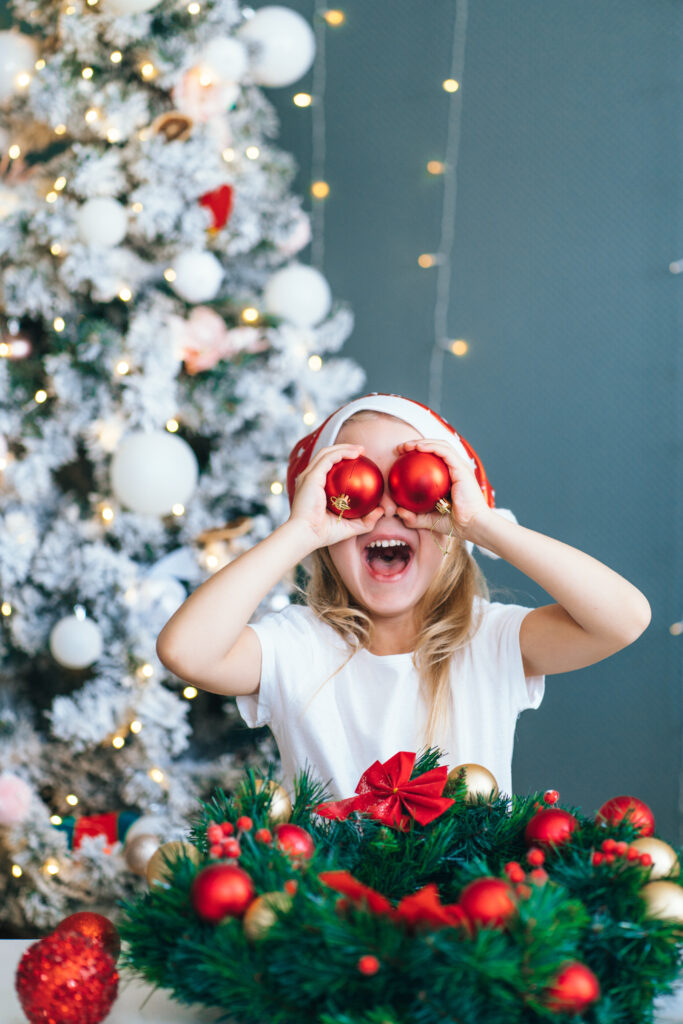 Decorative Image: Santa little helper with decorative Christmas tree on background. Little girl have fun play with red balls. Christmas and new year concept.